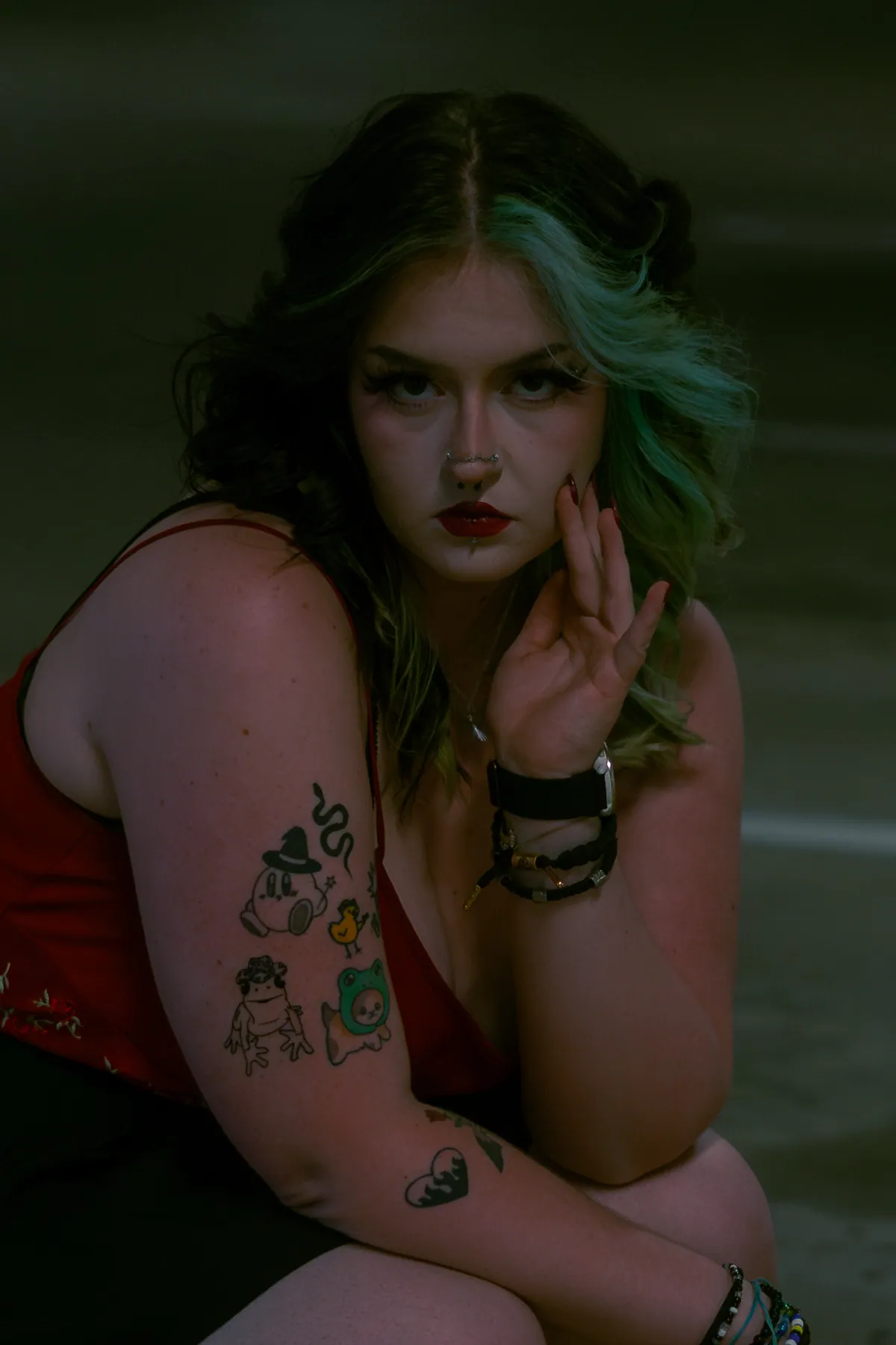 Moody portrait of a person with green-tinted hair resting her chin on her hand