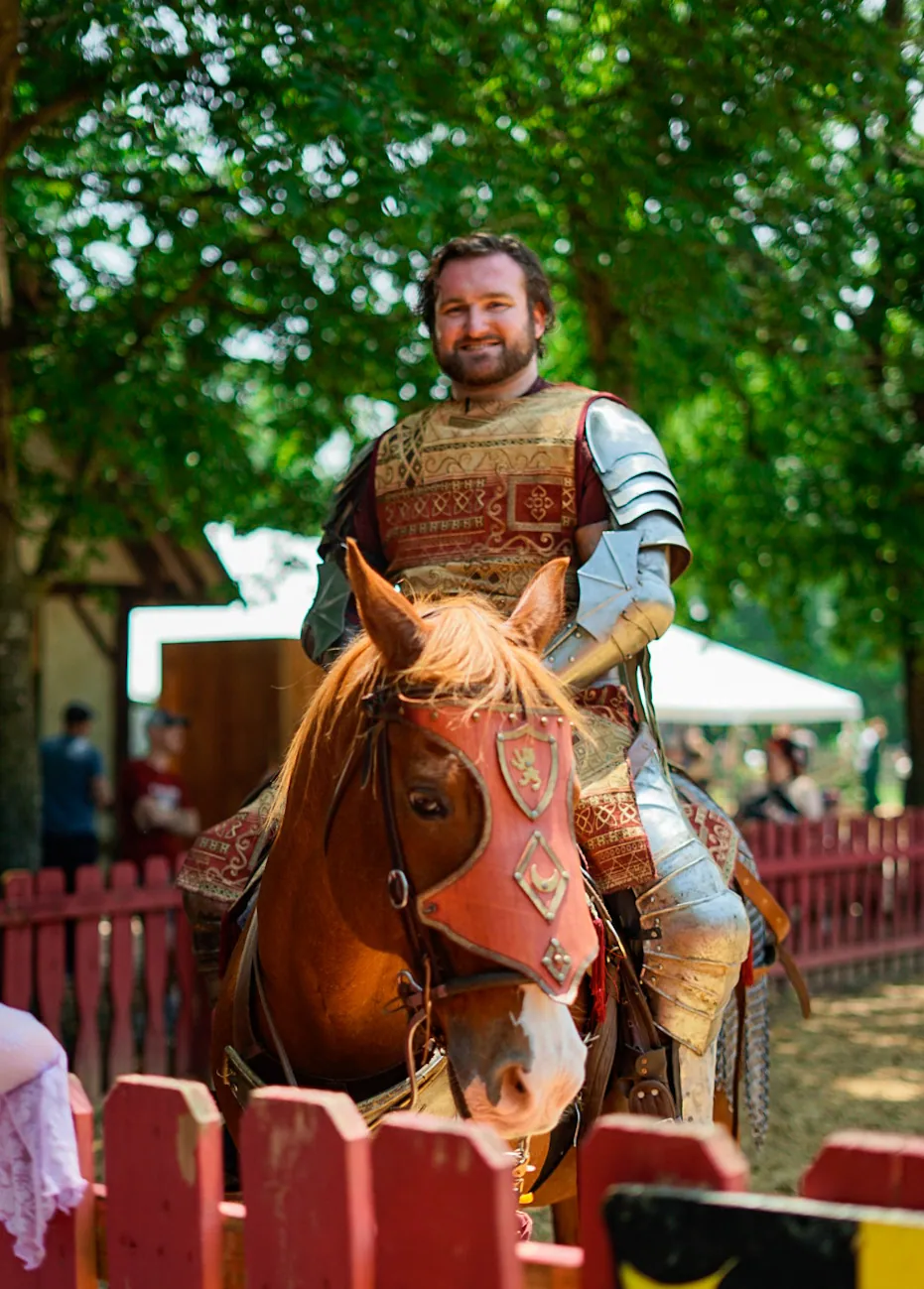 Costumed knight on a decorated horse behind a red fence at a Renaissance fair