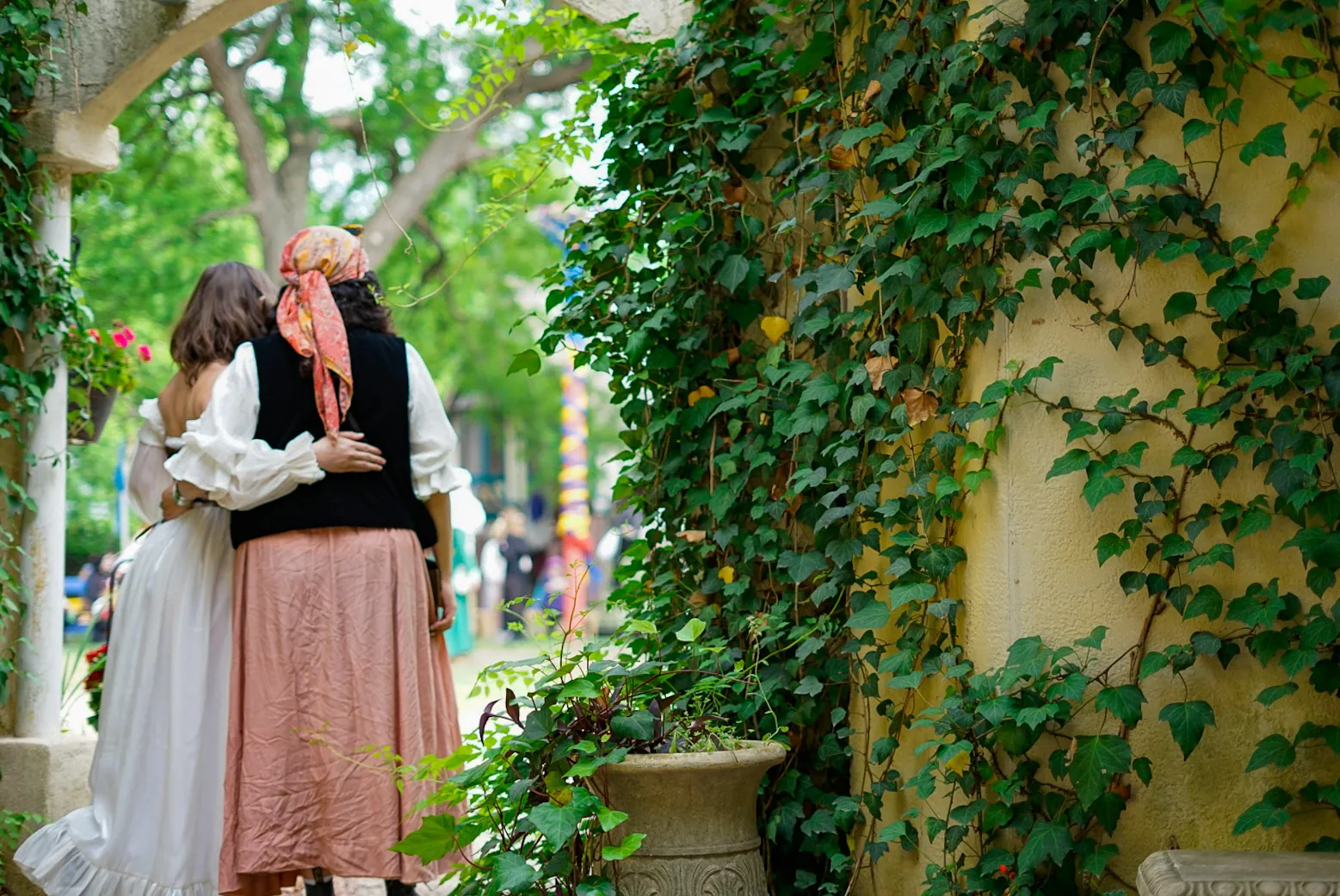 Two people in period costume embracing beside an ivy-covered wall